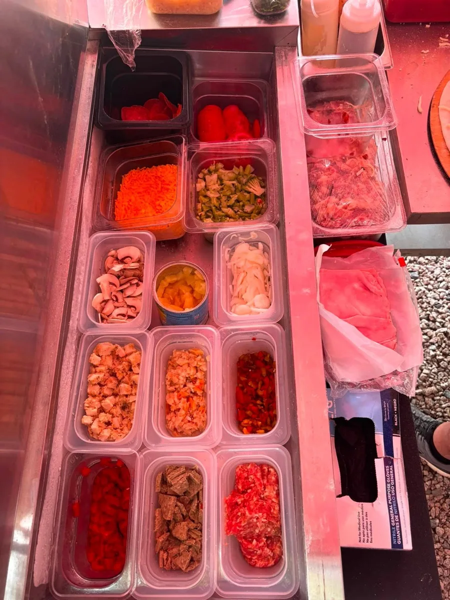 Fresh cut vegetables, meats and cheeses in the topping cooler of the Rollin Dough mobile pizza trailer